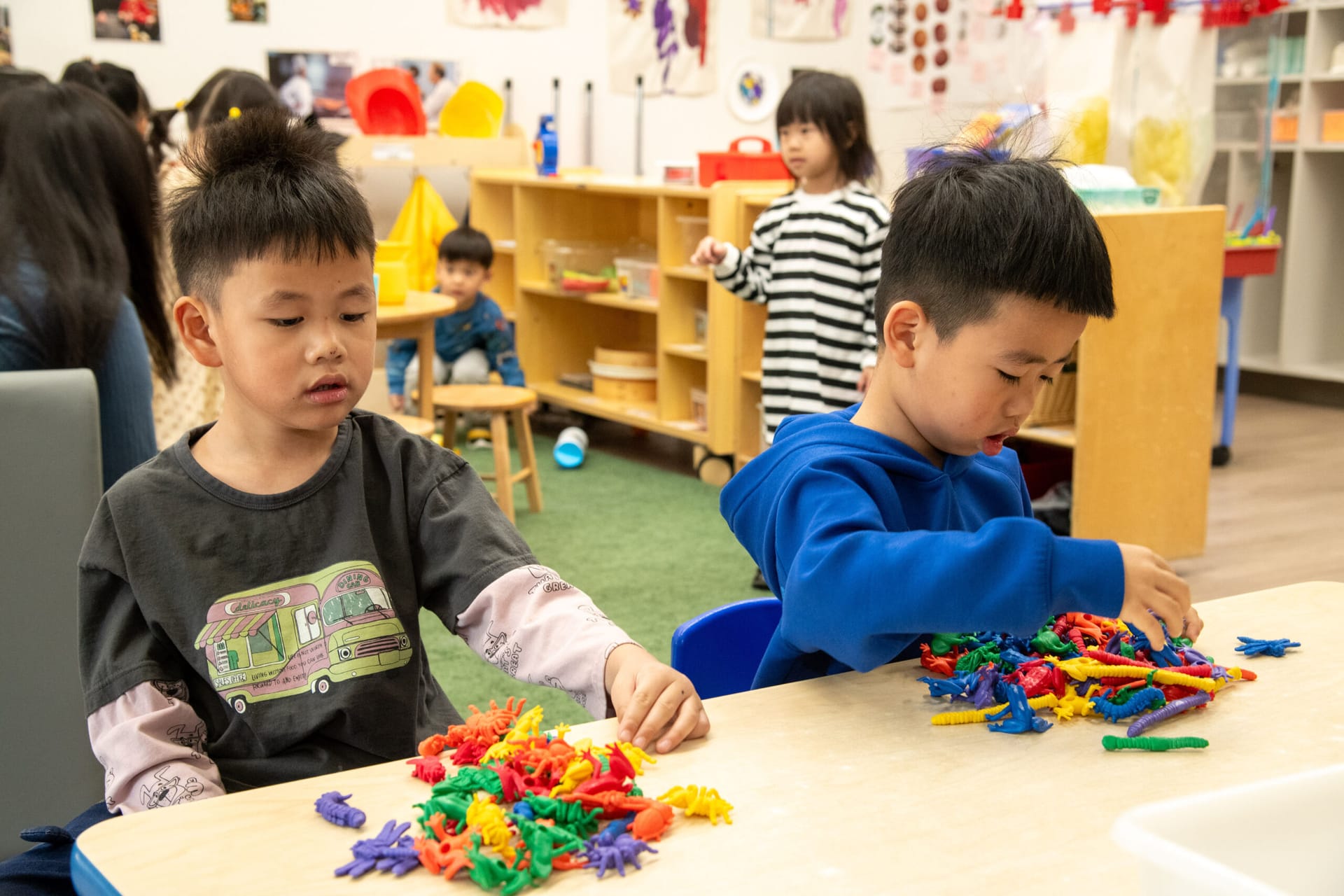 Two boys playing with plastic bugs and worms and spiders and frogs in a classroom
