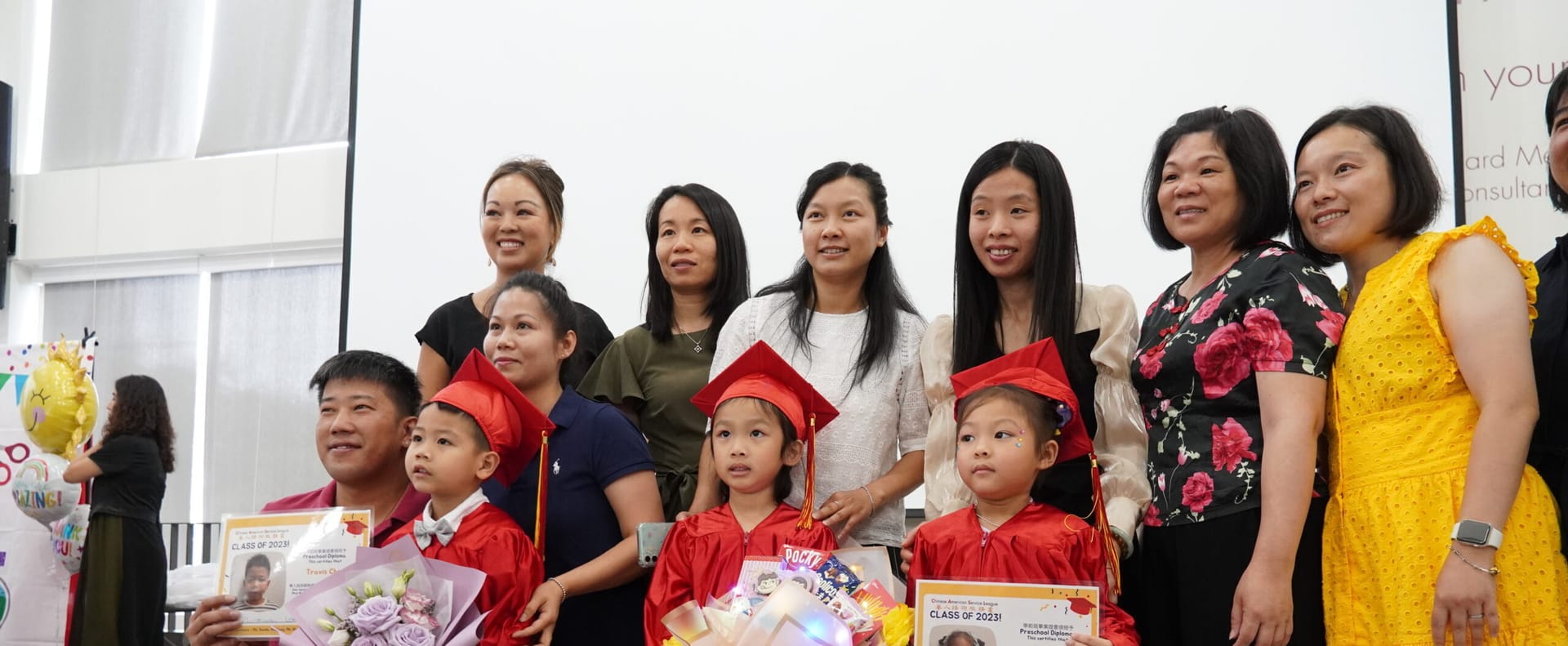 CASL Child Development Center children in red graduation caps and gowns, with parents and teachers.